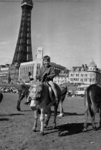 Photograph of a child enjoying a Blackpool donkey on the beach infront of the Blackpool tower